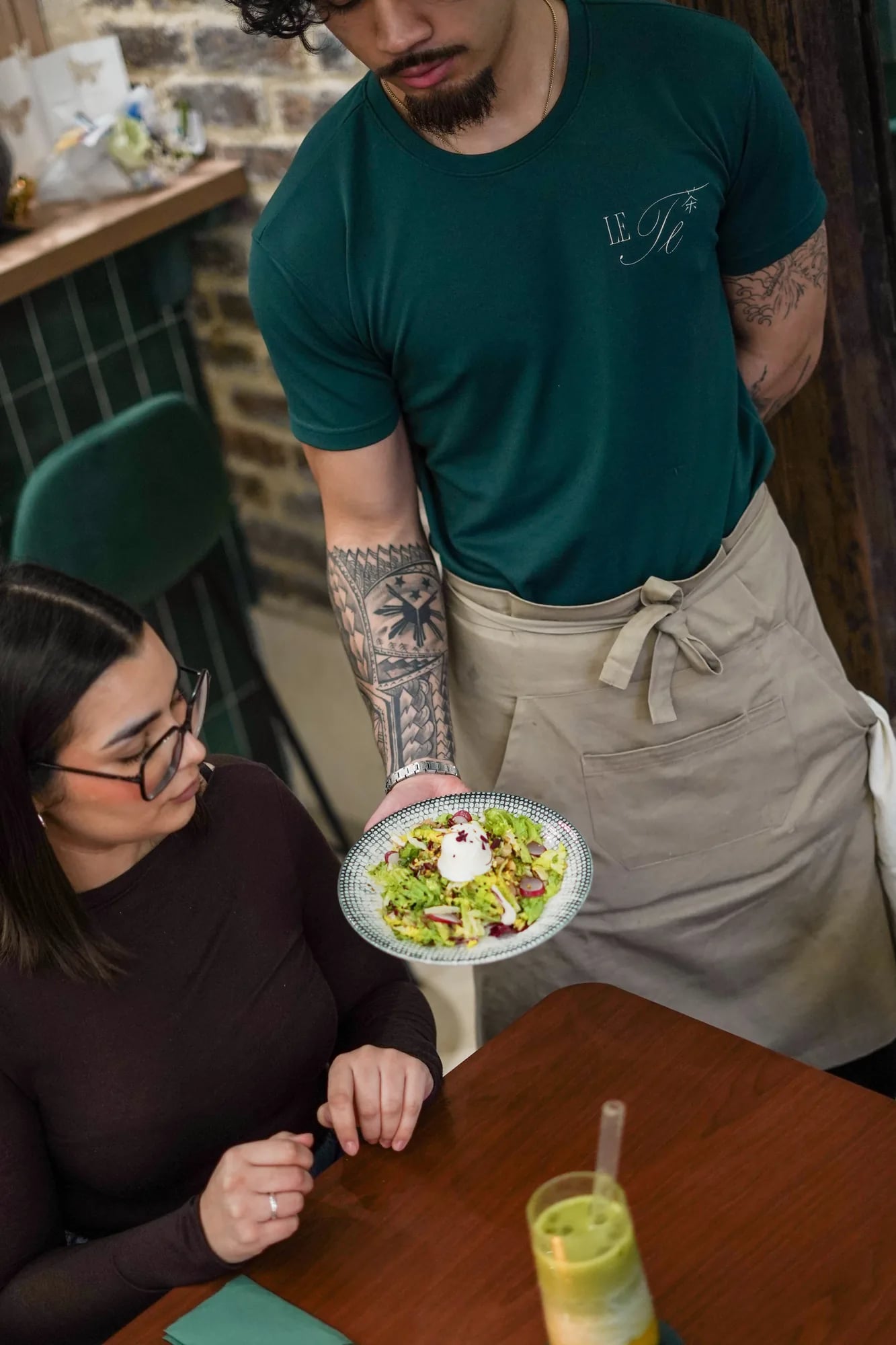 Serveur Le Te tatoue sert salade a cliente, t-shirt vert logo