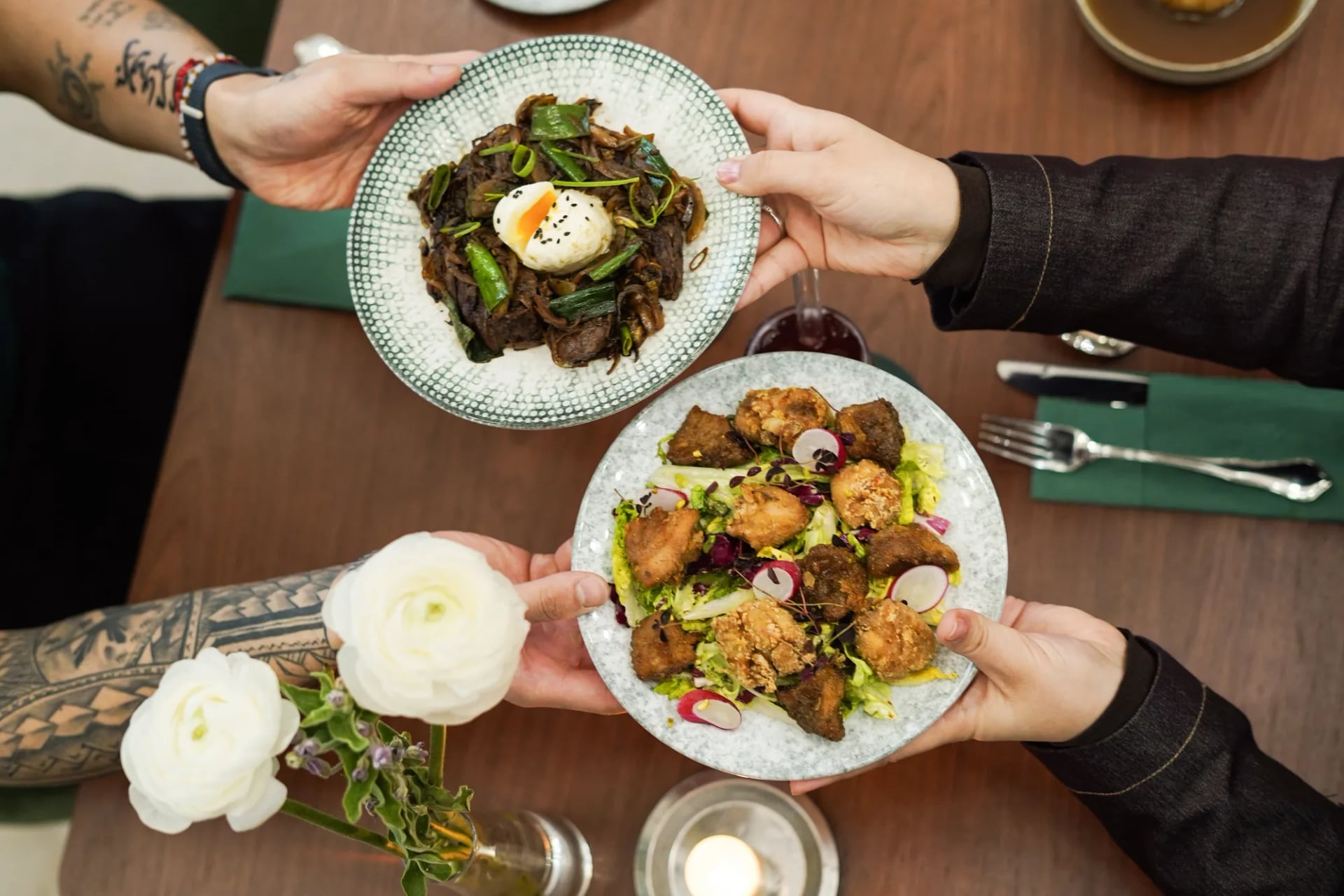Deux mains presentent assiettes top down, decor floral et tatouages