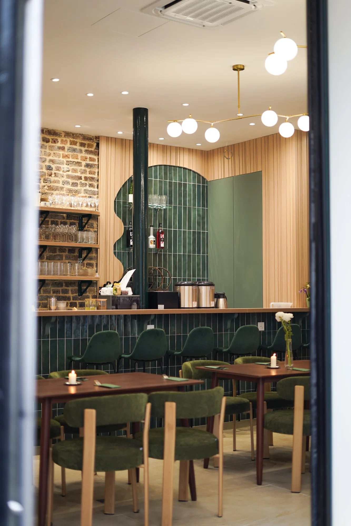 Vue salle depuis l'entrée vitrée, bar carrelé vert, suspensions globes laiton, chaises velours vert